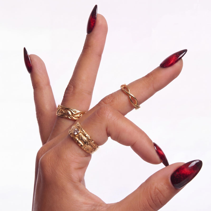 Hand model wearing Bloody Tears press-on nails with glossy black bases, deep red cat eye shimmer, smoky blood-red gradient, almond shapes, and gold rings