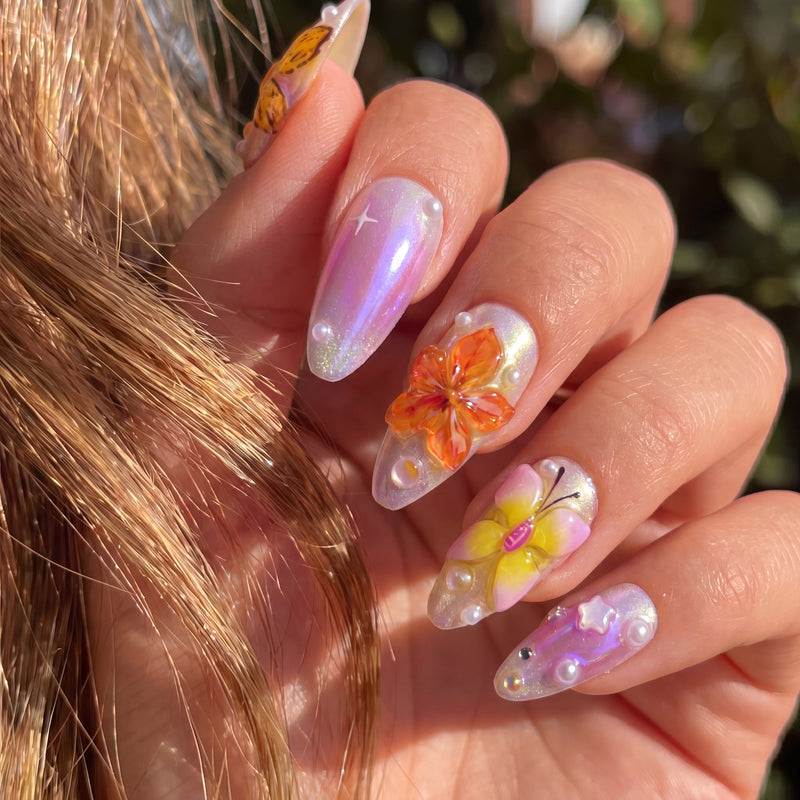 Close-up of Bloom Pop glossy pink press-on nails with an orange flower, yellow butterfly, pearls and star details