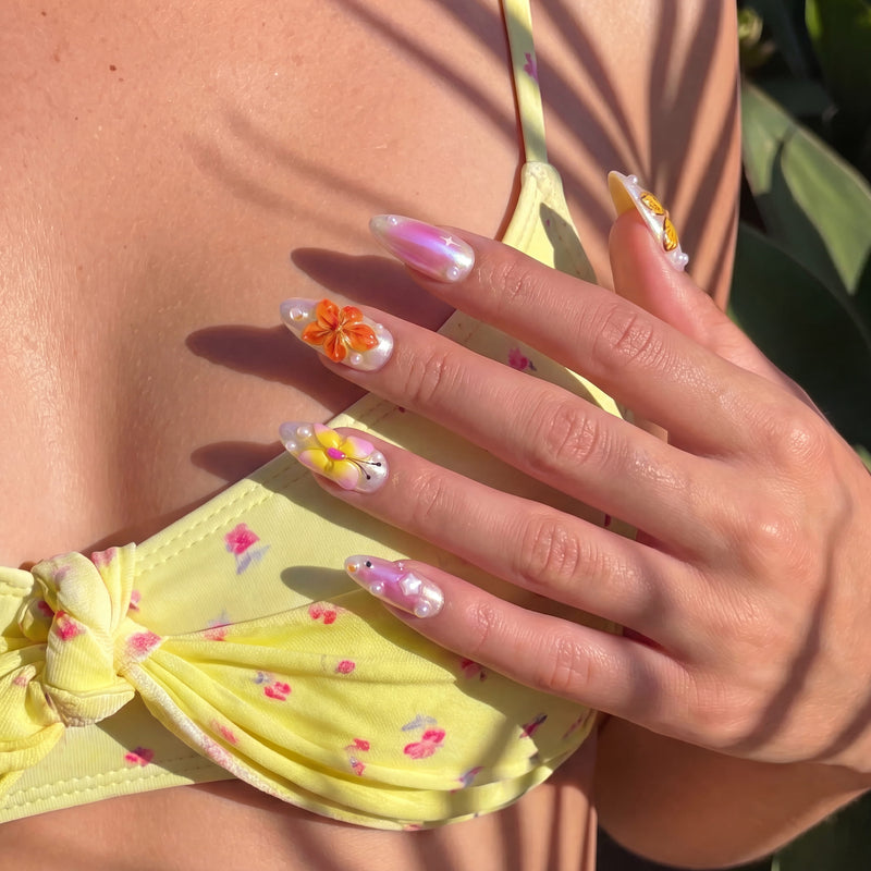 Model wearing Bloom Pop pink floral and butterfly press-on nails with a yellow floral top in warm sunlight