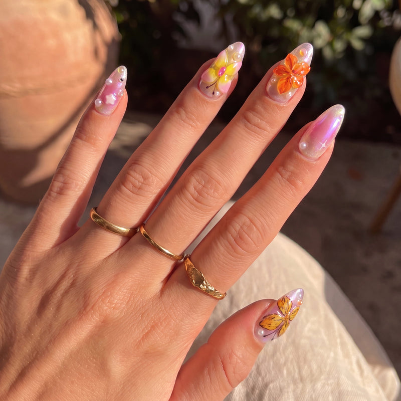 Hand model wearing Bloom Pop pink press-on nails with colorful raised flowers, butterflies and pearls in sunlight