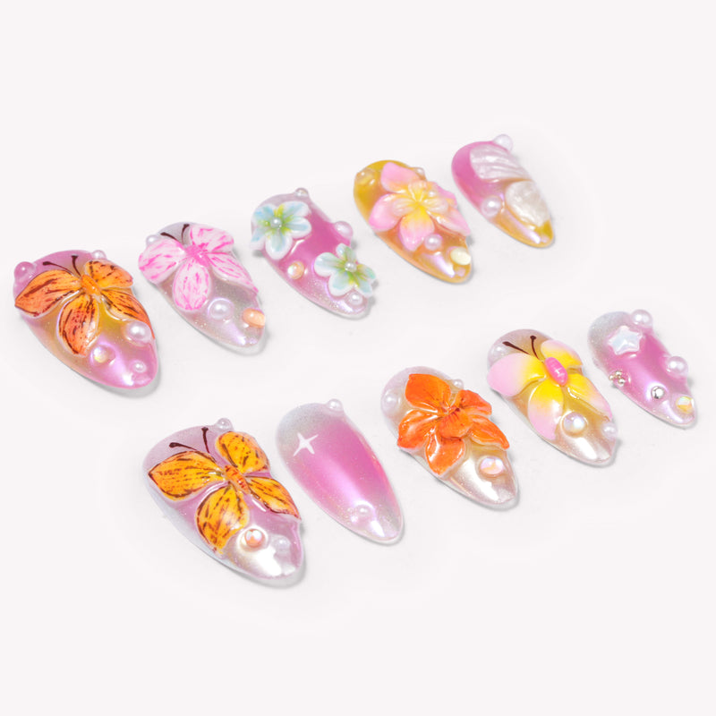Angled flat lay of Bloom Pop pink press-on nails with raised butterflies, colorful flowers, pearls and shimmer