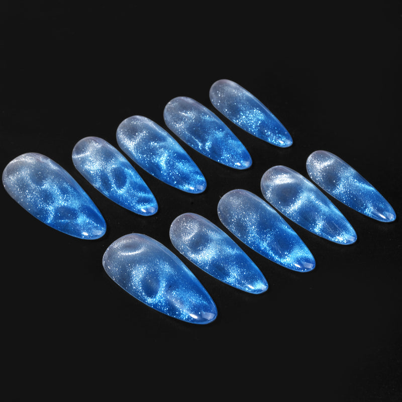 Blue Mirage blue and silver cat-eye almond press-on nails arranged in a sparkling black background flat lay
