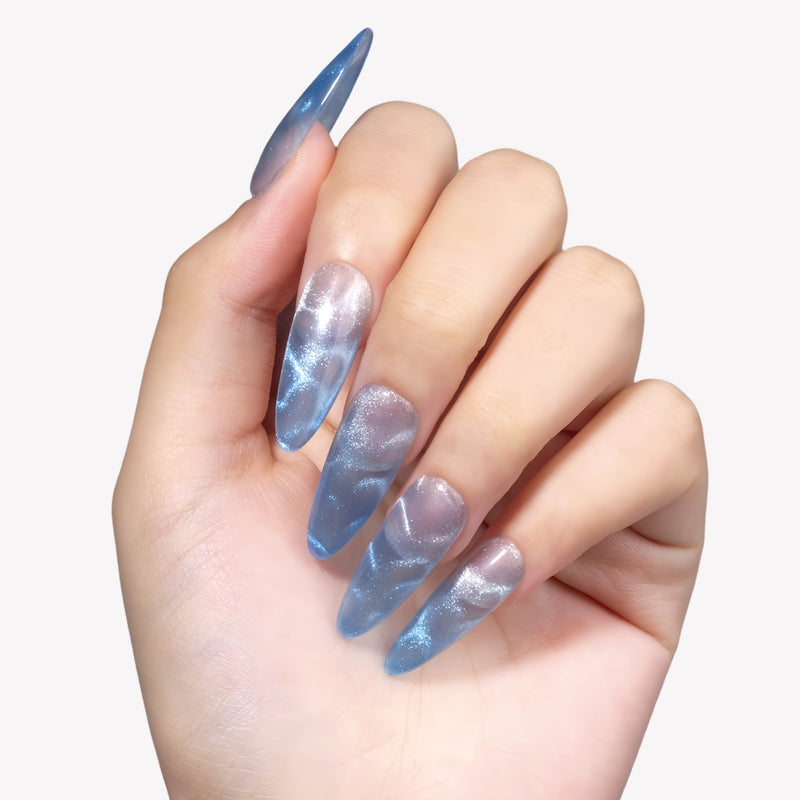 Blue Mirage long almond press-on nails with blue and silver cat-eye shimmer shown on a hand model