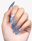 Blue Mirage long almond press-on nails with blue and silver cat-eye shimmer shown on a hand model
