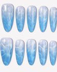 Blue Mirage press-on nails with a sky blue to white gradient, glossy cat-eye shimmer, and soft water-ripple effect