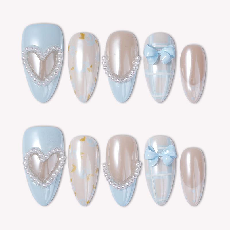 A set of 10 almond-shaped press-on nails in soft baby blue and creamy nude with coquette-style 3D pearl heart charms, light blue bow accents, pearl dividers, blue plaid patterns, and delicate floral accents, displayed in two rows on a white background