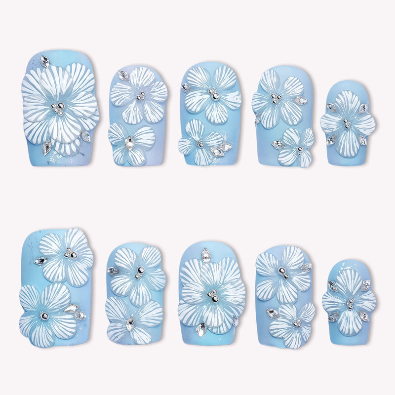 A set of sky blue press-on nails with white floral petals and rhinestone accents on a white background