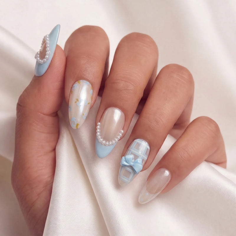 Hand model wearing baby blue and nude press-on nails with pearl hearts, bows, pearl trim, and gingham accents.