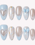 Flat lay of blue and nude press-on nails with pearl heart charms, bows, pearl borders, and soft gingham accents on a white background.