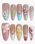 Flat lay of multicolor floral press-on nails with pastel blue, pink, yellow, and burgundy flower details on a white background.