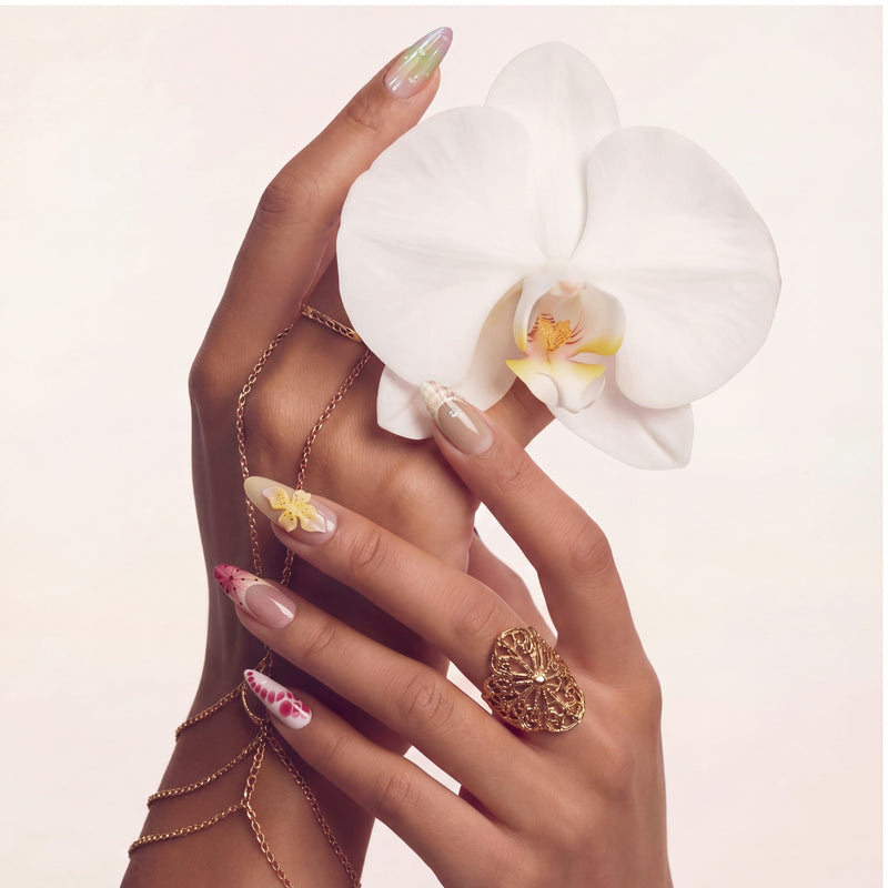 Hand model wearing multicolor floral press-on nails with a large white orchid accent and gold jewelry.