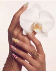 Hand model wearing multicolor floral press-on nails with a large white orchid accent and gold jewelry.