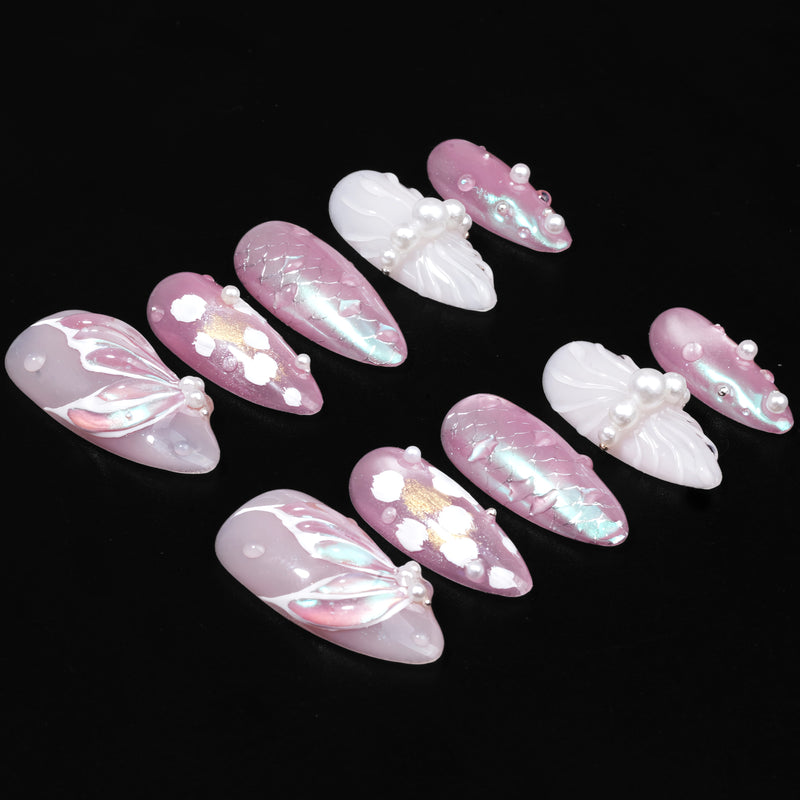Pink and white press-on nails with pearl accents arranged on a black background.