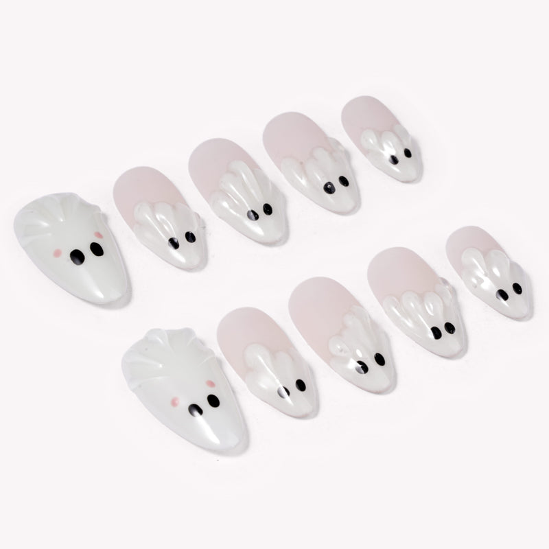 Angled flat lay of Boo Cuties press-on nails with pale pink bases, glossy white ghost tips, black eyes, and soft pink cheek dots