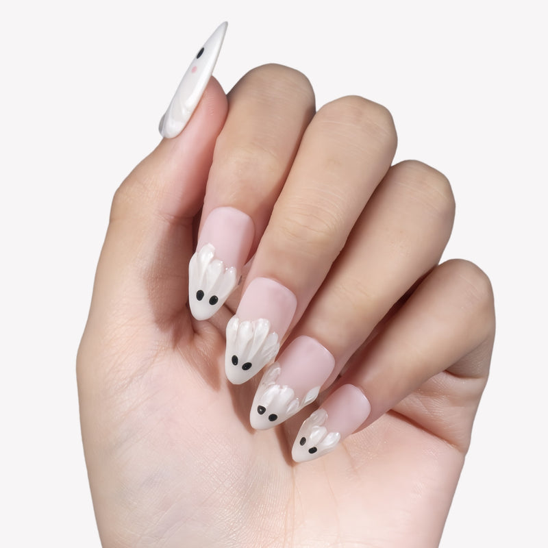 White background hand model wearing Boo Cuties press-on nails with pale pink bases, raised white ghost tips, and black eye details