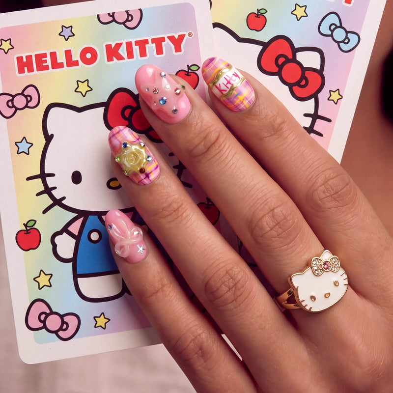 Hand model wearing Bubblegum Pop Arcade handmade press-on nails with pink plaid, gems, gold accents, and Hello Kitty styling.