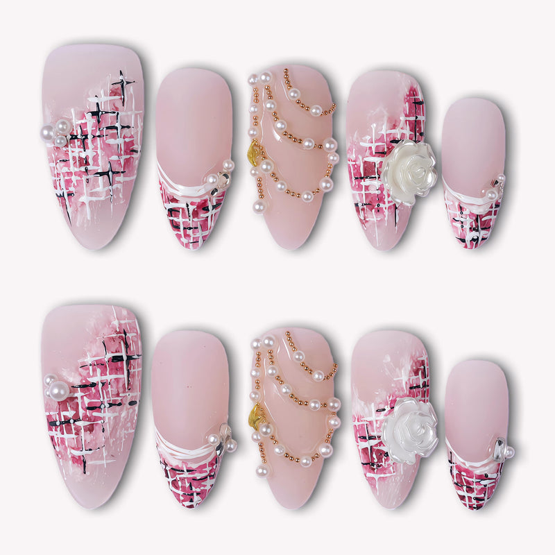 Flat lay of pink nude press-on nails with tweed plaid tips, pearl accents, gold chains, and a white rose charm