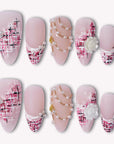 Flat lay of pink nude press-on nails with tweed plaid tips, pearl accents, gold chains, and a white rose charm