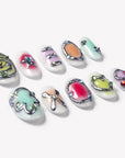 Flat lay of Candy Chrome press-on nails with silver chrome outlines, pastel heart star and bow designs, glossy candy colors, and rhinestone details