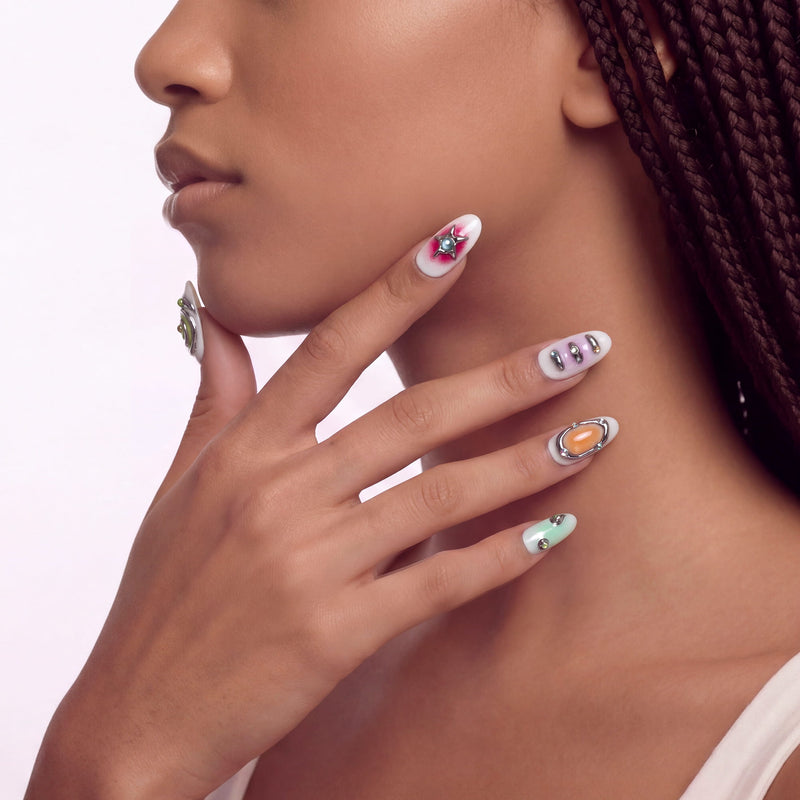 Side face close-up hand model wearing Candy Chrome press-on nails with silver chrome outlines, pastel star and heart designs, glossy accents, and rhinestones