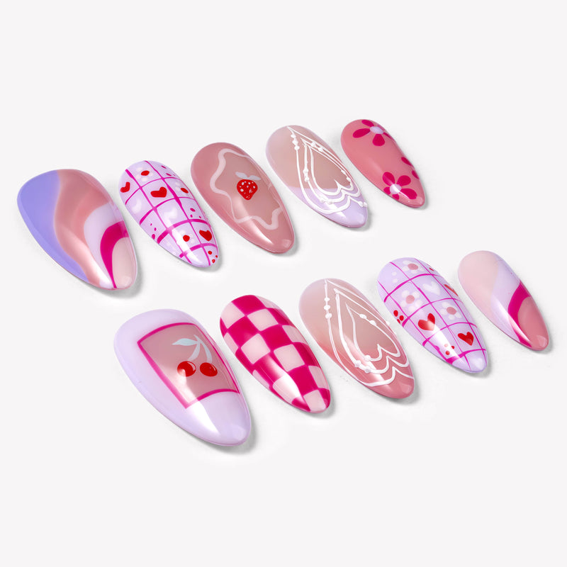 Angled flat lay of Candy Crush press-on nails with pink and purple tones, heart grid patterns, cherries, flowers, swirls, and white line art details