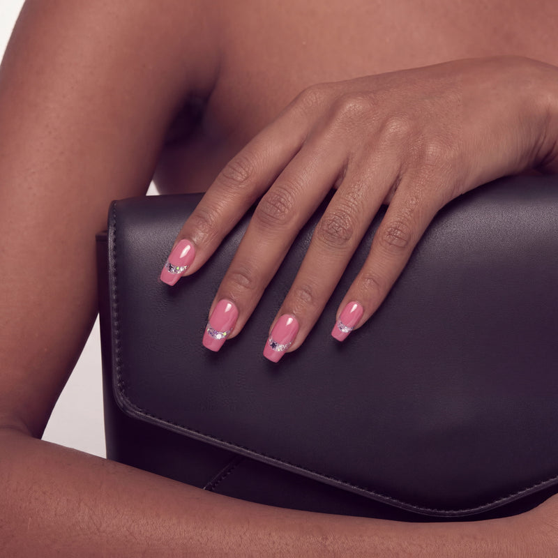 Hand model wearing Candy Spark pink press-on nails resting on a black clutch bag