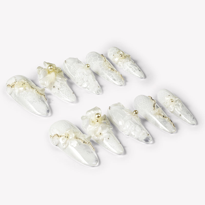 Celeste white floral press-on nails with lace patterns, pearls and gold beads arranged in an angled flat lay