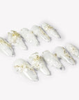 Celeste white floral press-on nails with lace patterns, pearls and gold beads arranged in an angled flat lay