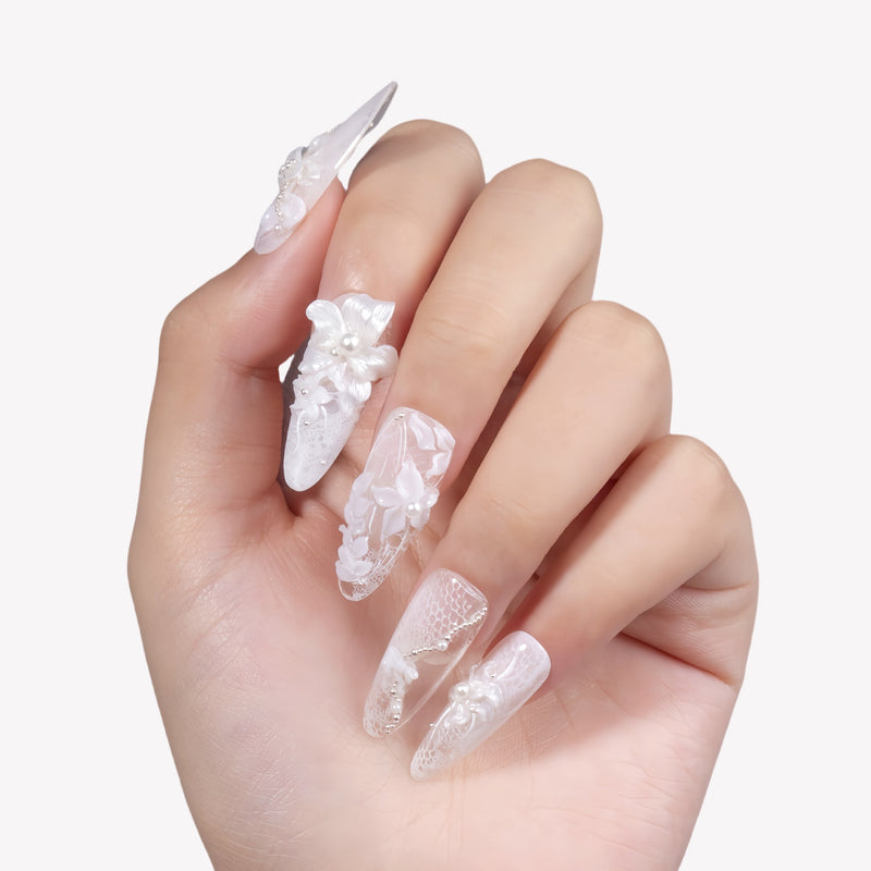 Hand model wearing Celeste white lace floral press-on nails with sculpted flowers and pearl accents on a white background