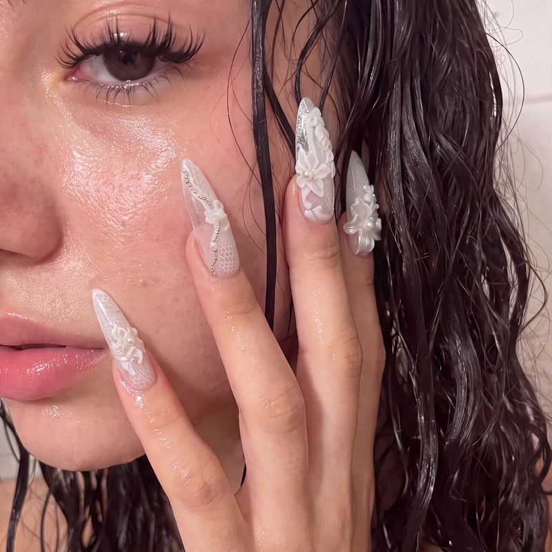 Close-up model wearing Celeste white floral stiletto press-on nails with pearl details in a wet-look beauty shot