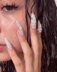 Close-up model wearing Celeste white floral stiletto press-on nails with pearl details in a wet-look beauty shot