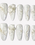 Celeste white floral press-on nails with pearl and gold bead accents arranged in a clean flat lay