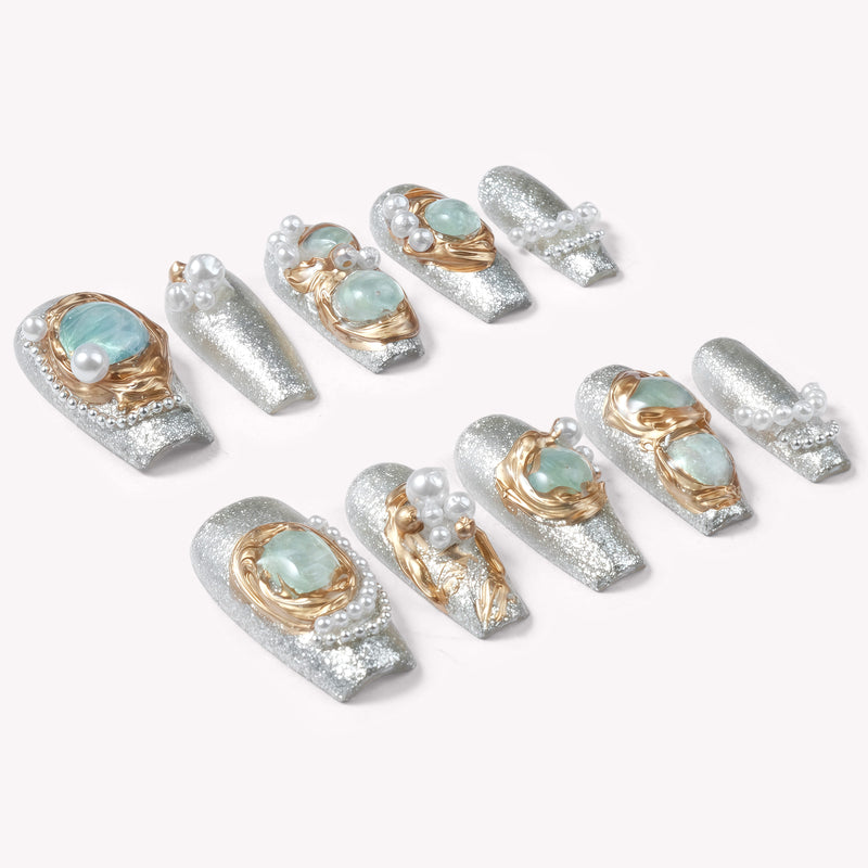 Individual Celestial Tide press-on nails arranged on a white background with silver glitter, gold swirls, pale blue stones, and pearl accents
