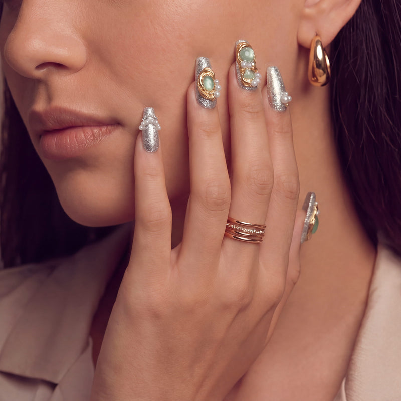 Portrait close-up of a hand model wearing Celestial Tide press-on nails with silver glitter, gold swirls, and pearl accents