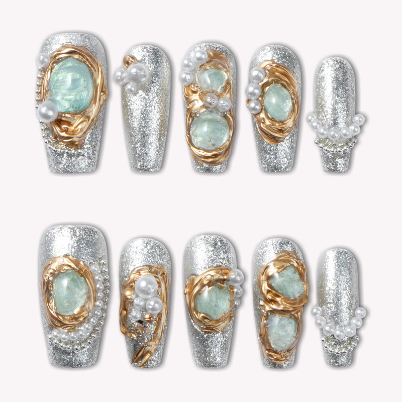 Celestial Tide press-on nails in silver glitter with gold swirls, pale blue stones, and pearl accents arranged in a flat lay