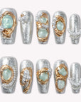 Celestial Tide press-on nails in silver glitter with gold swirls, pale blue stones, and pearl accents arranged in a flat lay