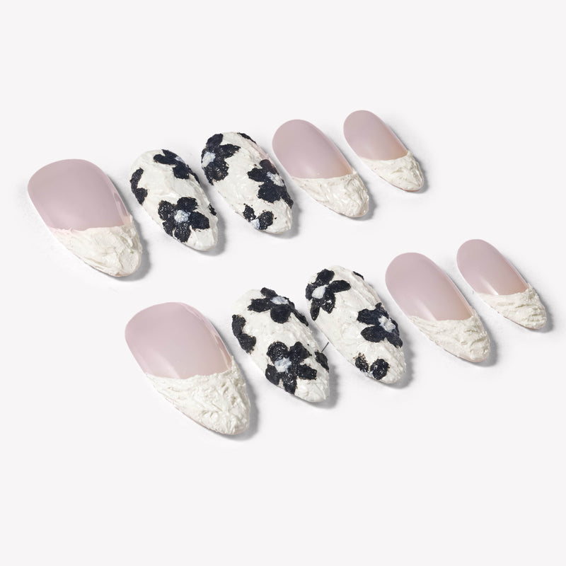 Angled flat lay of Chalk Floral press-on nails with nude pink bases, textured white French tips, and black floral accents