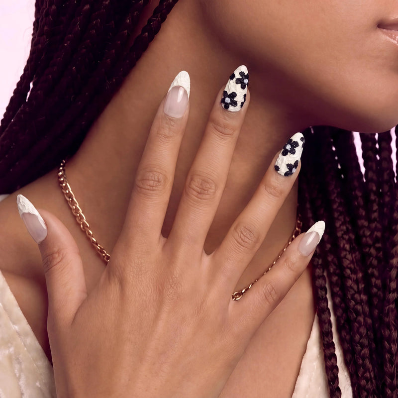 Hand model wearing Chalk Floral press-on nails with nude pink bases, textured white tips, and raised black flower accents