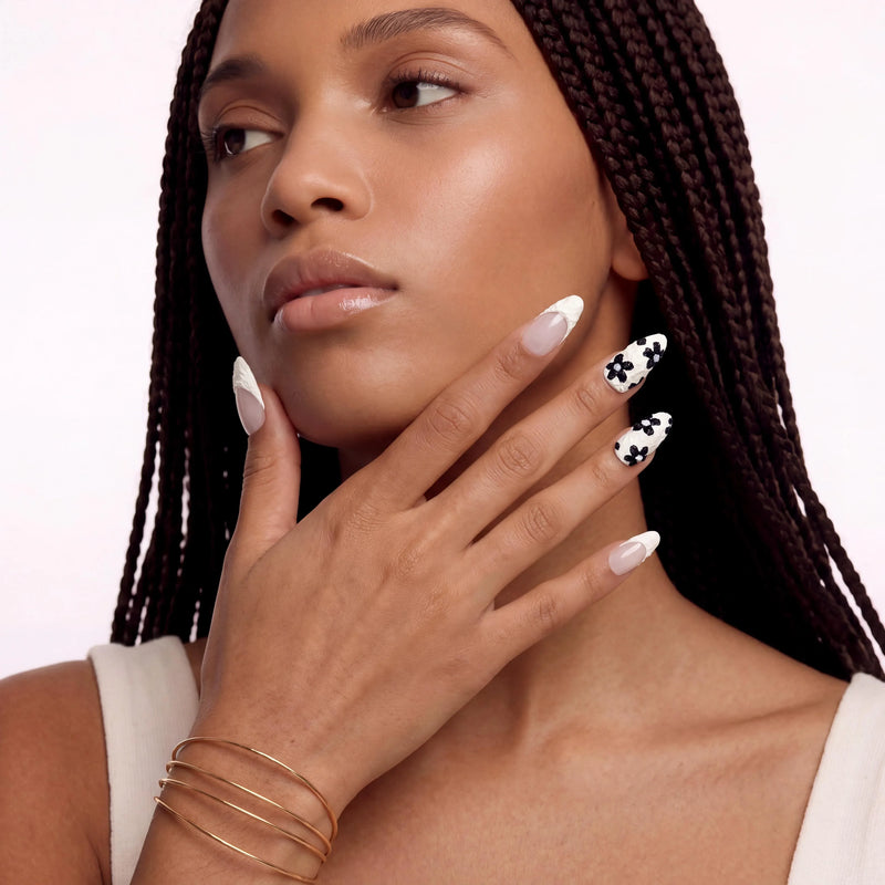 Portrait hand model wearing Chalk Floral press-on nails with nude pink bases, textured white tips, and raised black floral accents