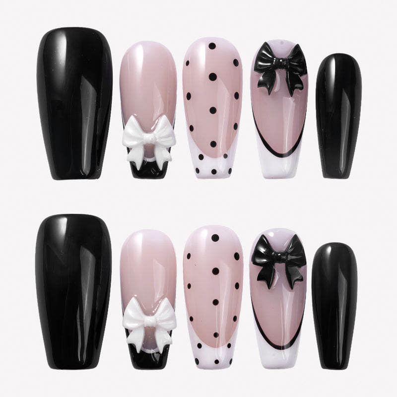 Chérie Noir press-on nails with glossy black nails, nude pink bases, black polka dots, black French outline, and raised black and white bow designs