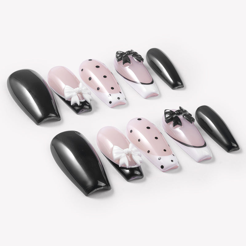 Flat lay of Chérie Noir press-on nails with glossy black nails, nude pink bases, black polka dots, black French outline, and raised black and white bow designs