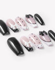 Flat lay of Chérie Noir press-on nails with glossy black nails, nude pink bases, black polka dots, black French outline, and raised black and white bow designs