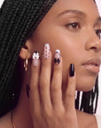Side face close-up hand model wearing Chérie Noir press-on nails with glossy black nails, nude pink polka dots, black French outline, and raised black and white bow accents