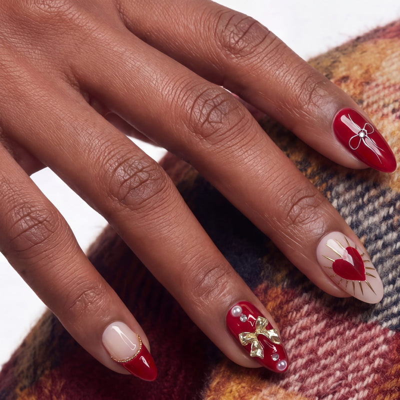 Close-up of a hand model wearing Cherry Devotion press-on nails in red, blush, and gold with cherries, bows, and hearts