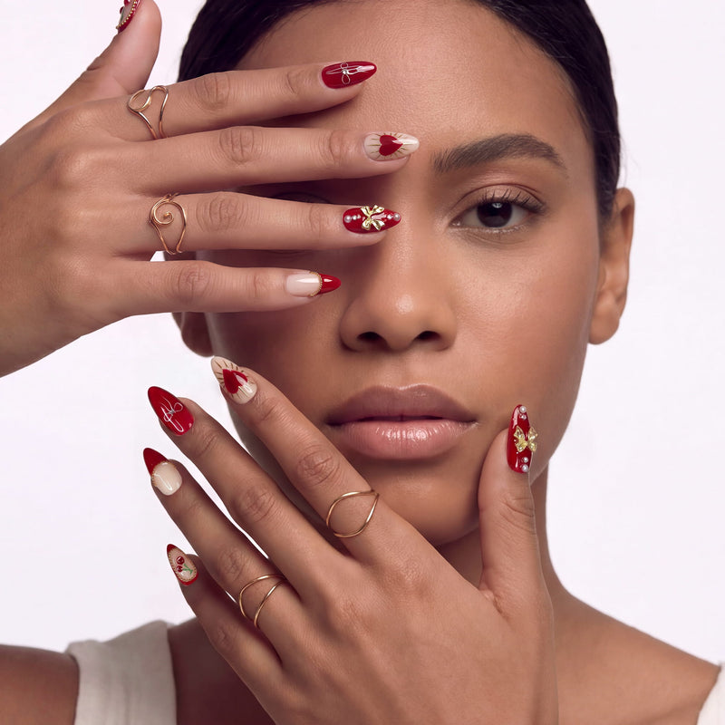 Lifestyle portrait of a hand model wearing Cherry Devotion press-on nails in red, blush, and gold with cherries, bows, and hearts