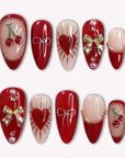 Cherry Devotion press-on nail set in red, blush, and gold with cherries, bows, hearts, and pearl accents arranged on a white background