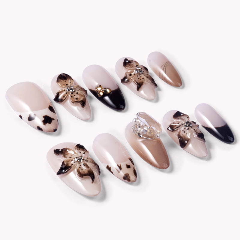Angled flat lay of Chestnut Bloom press-on nails with nude pink bases, brown floral petals, black French accents, and rhinestone details