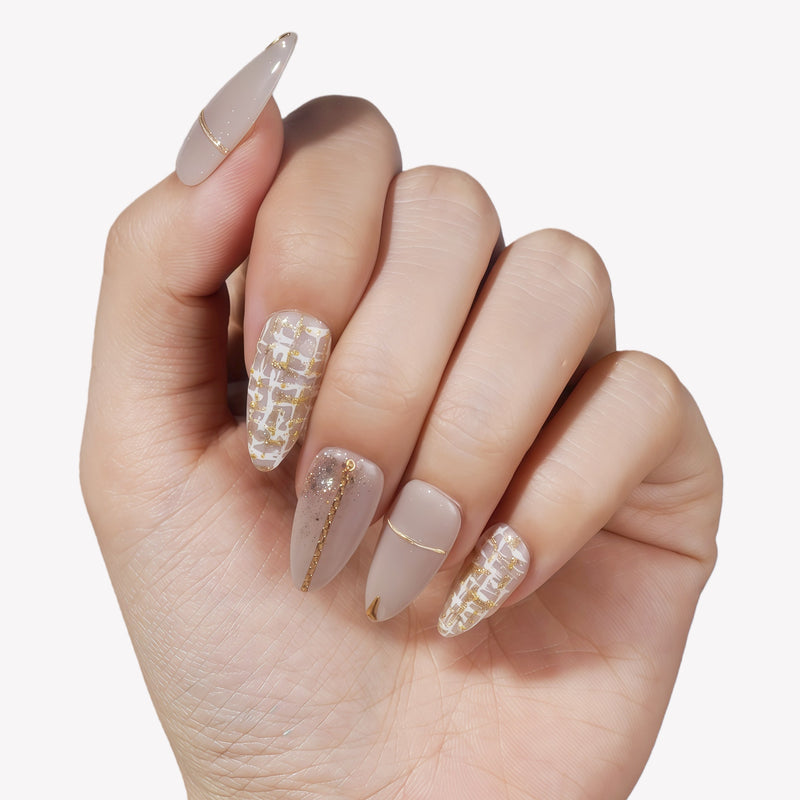 Hand model wearing beige press-on nails with gold line accents and tweed plaid details