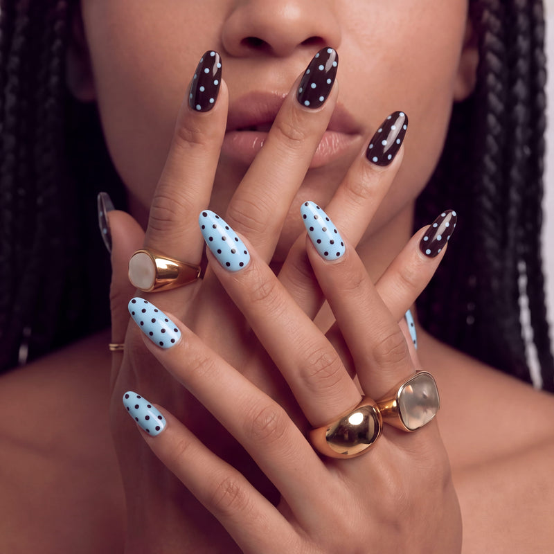 Close-up hand model near her face wearing Choco Sky Dots press-on nails with chocolate brown and sky blue polka dot designs plus gold rings