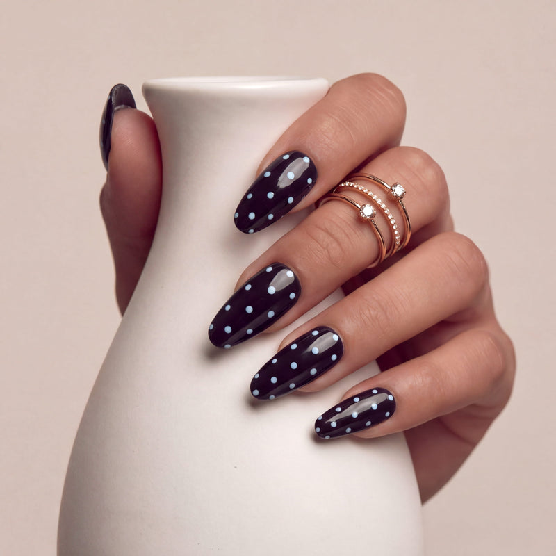 Hand model holding a white vase while wearing Choco Sky Dots press-on nails with glossy dark chocolate brown bases and blue polka dots